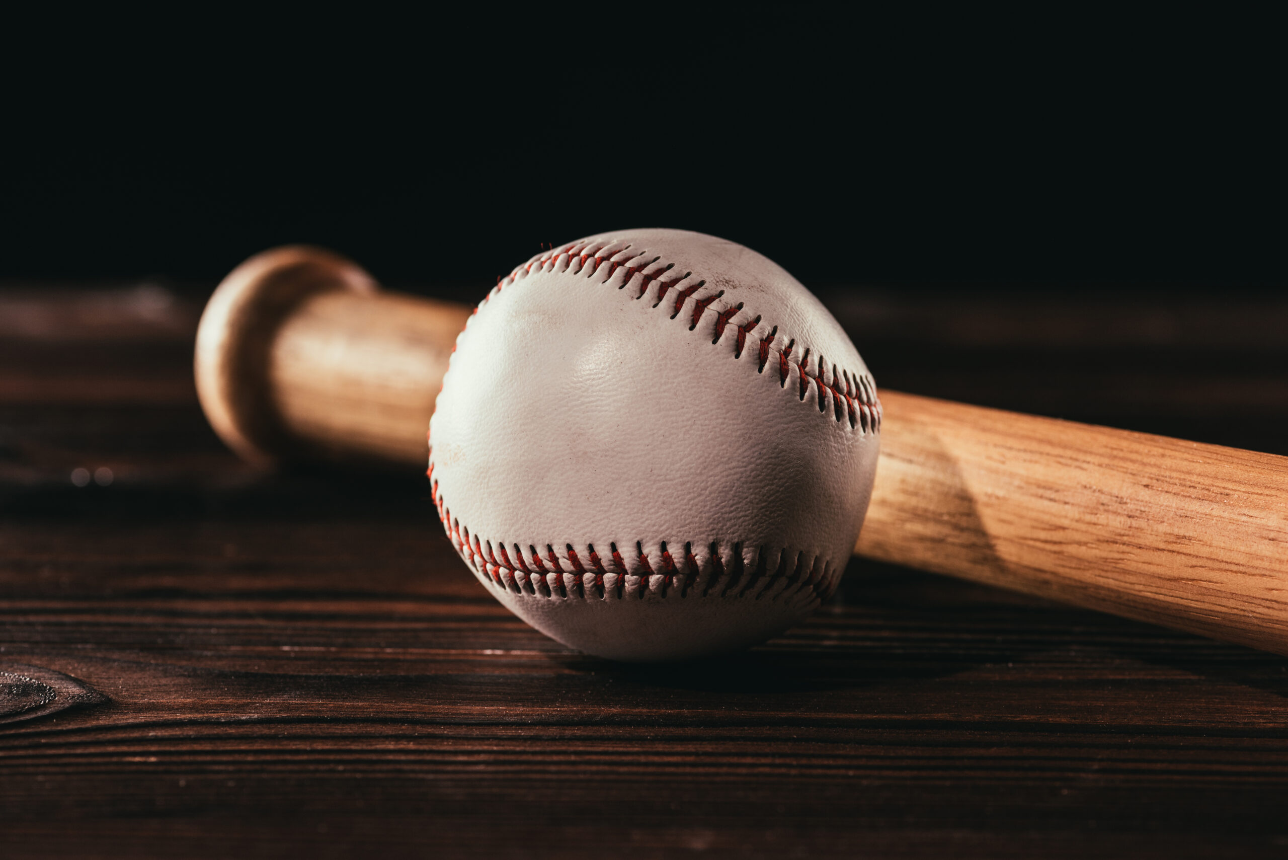 close-up view of white leather baseball ball and bat on wooden table